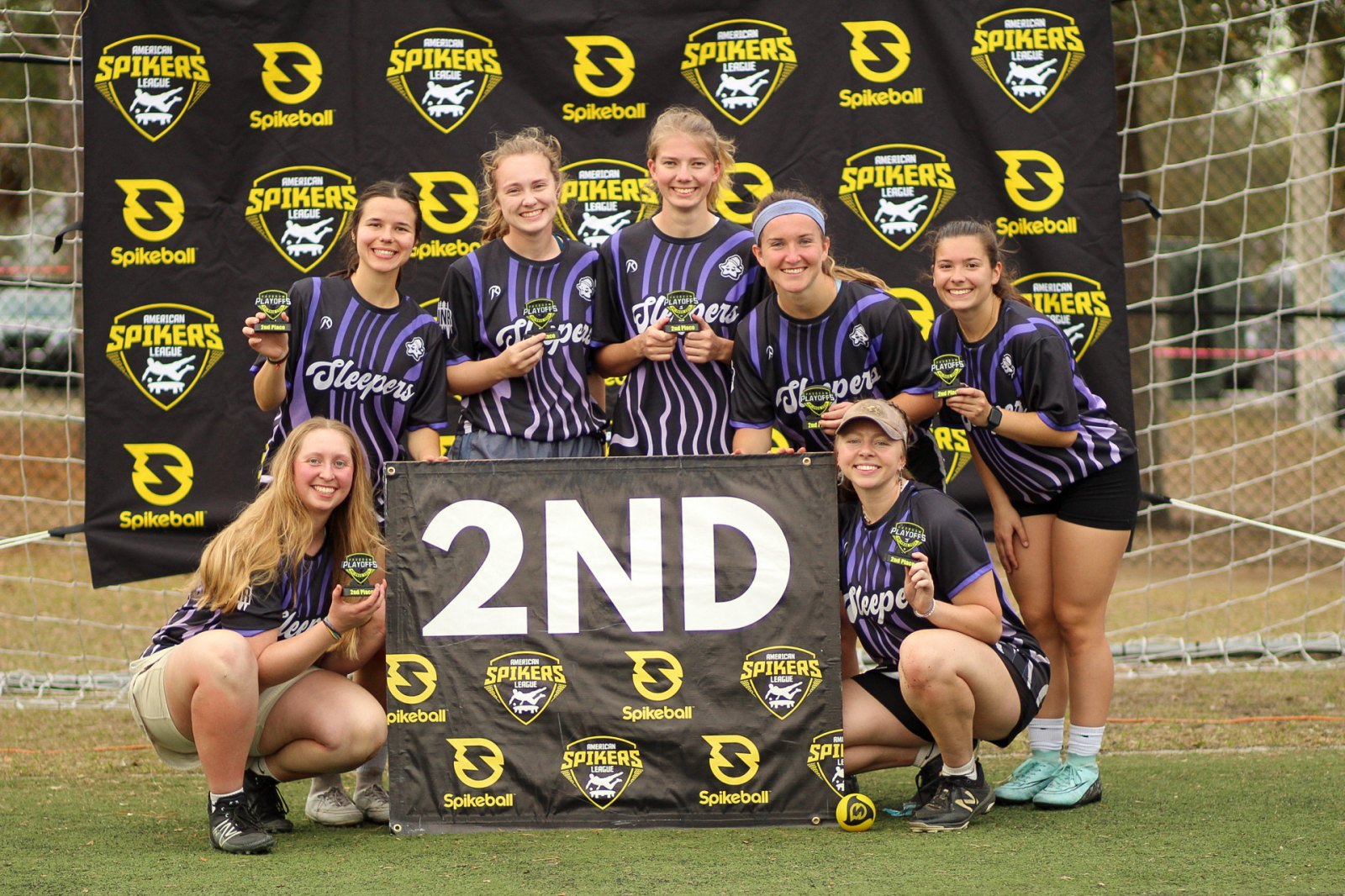 A women's squad on the podium with their 2nd place banner